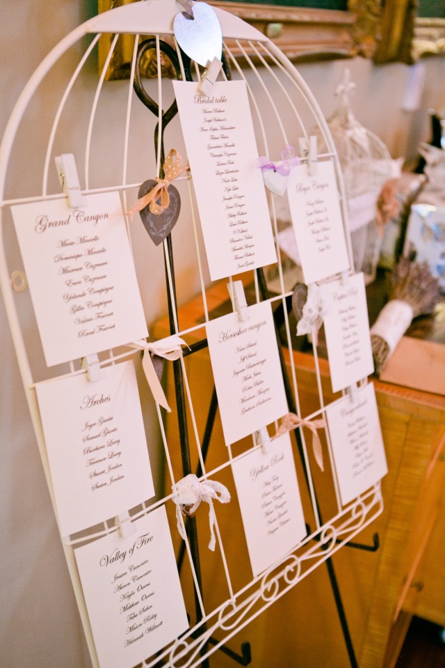 5x7 cards with guests listed are clipped to a large birdcage for a unique table seating assignment at a wedding