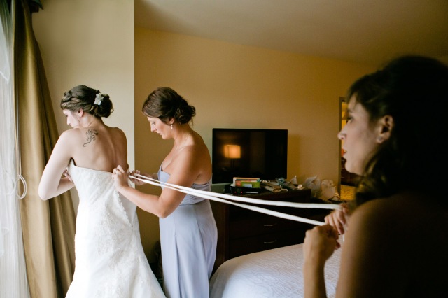 two bridesmaids help a bride get laced into her dress