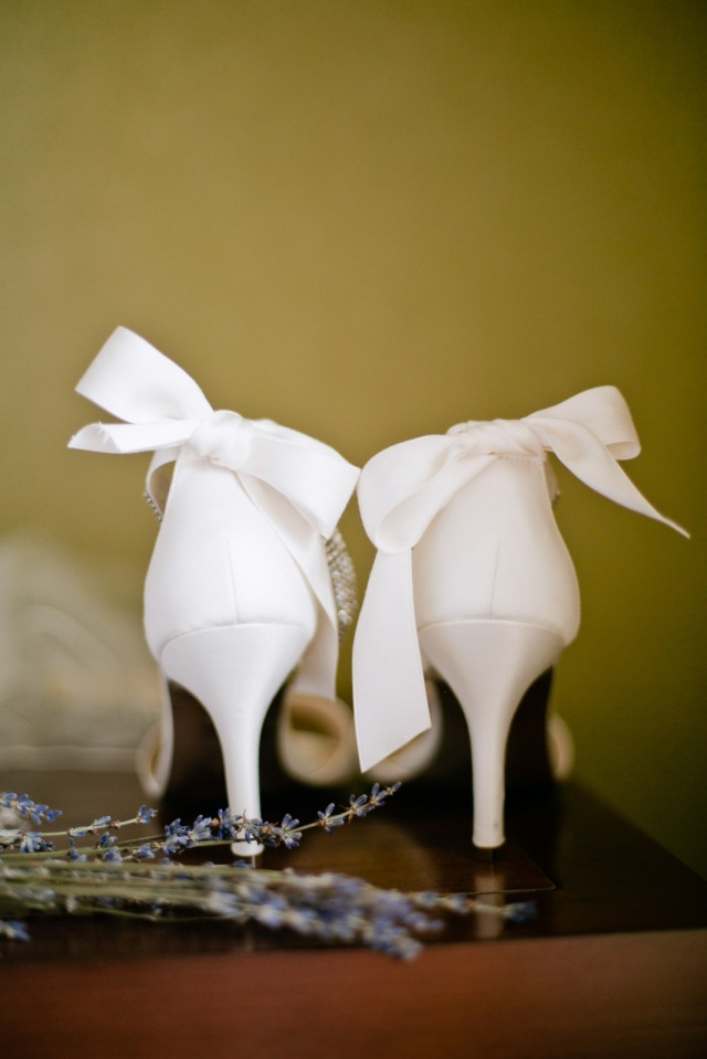 ivory bridal shoes complete with bows over the back of the shoe sit side by side. Design by Mina of New York